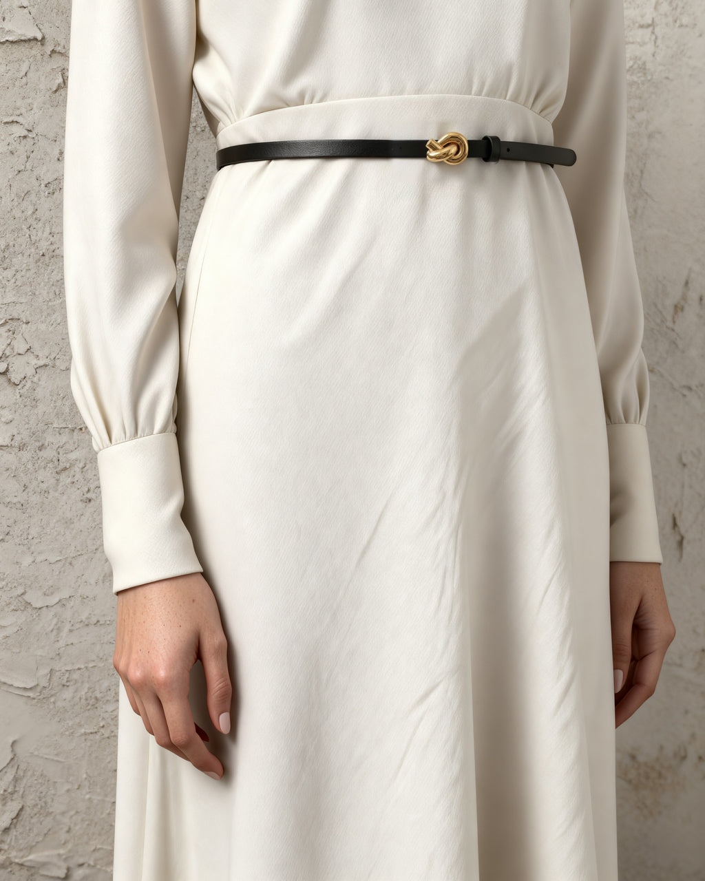 the line — the slim black belt with its gold knot buckle over a cream dress