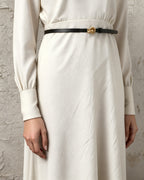 the line — the slim black belt with its gold knot buckle over a cream dress
