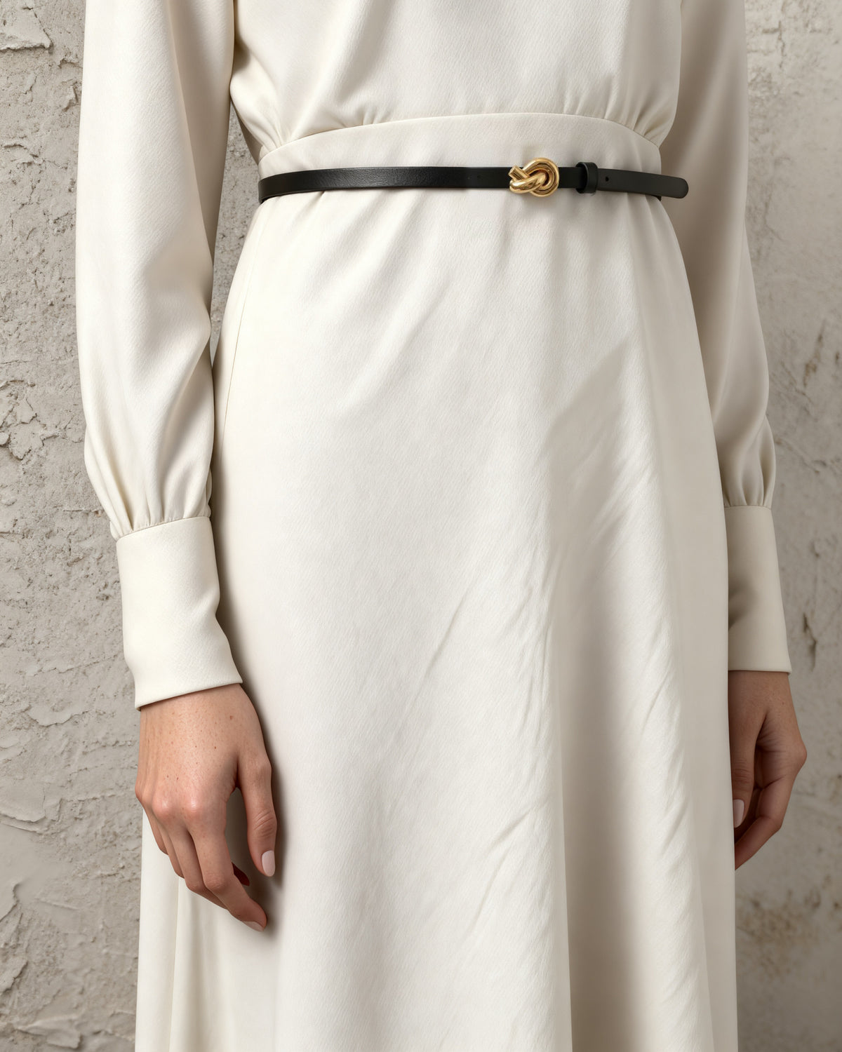 the line — the slim black belt with its gold knot buckle over a cream dress